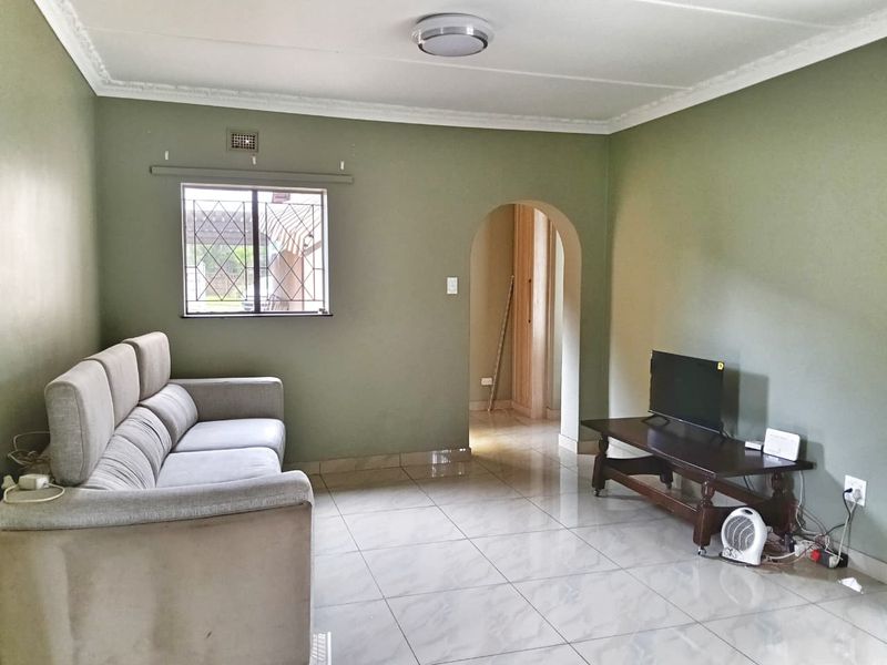 A living room featuring tiled flooring, an arched doorway leading to an adjacent space, and decorative ceiling cornicing.