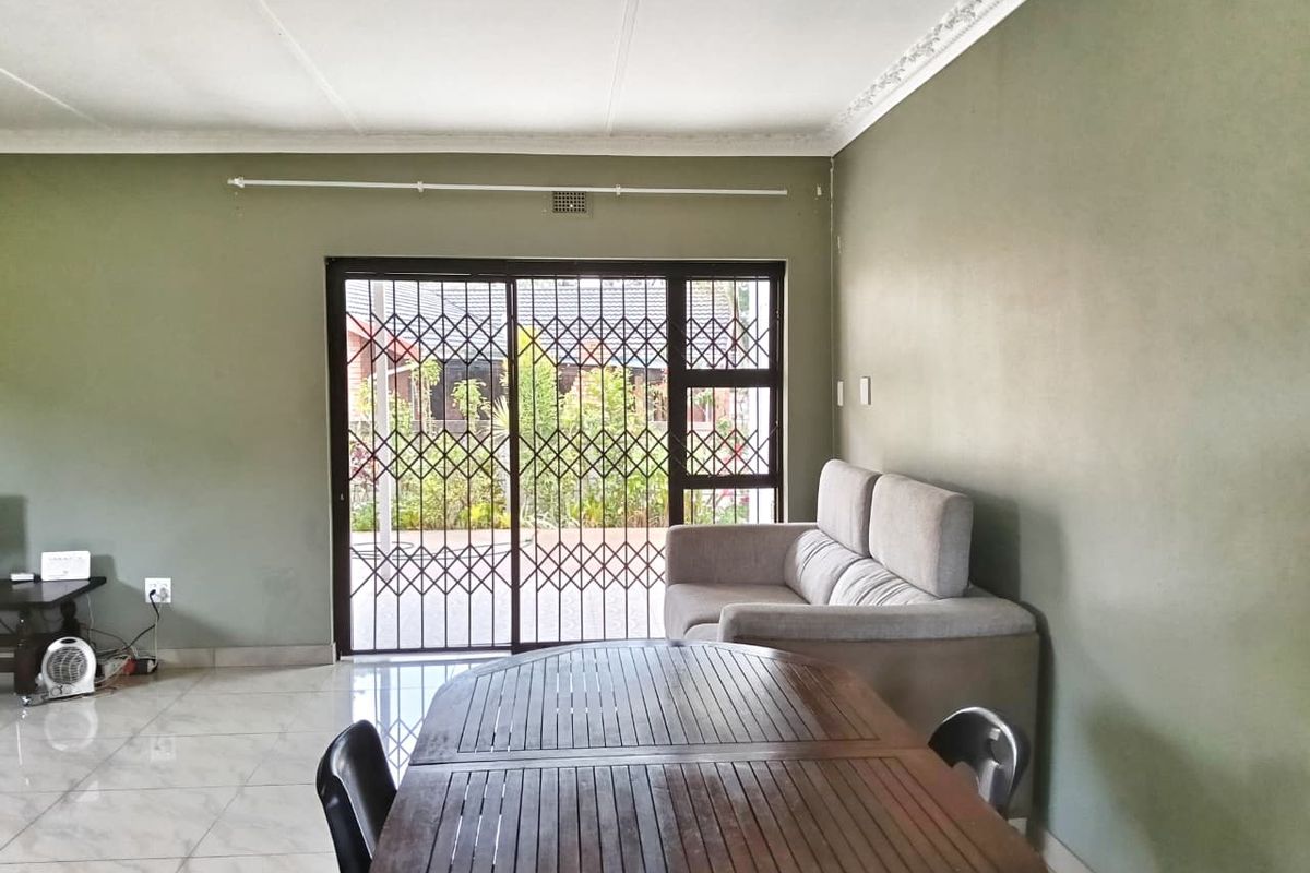 A living room featuring tiled flooring, decorative ceiling cornices, and a sliding glass door with a security gate leading to the exterior.