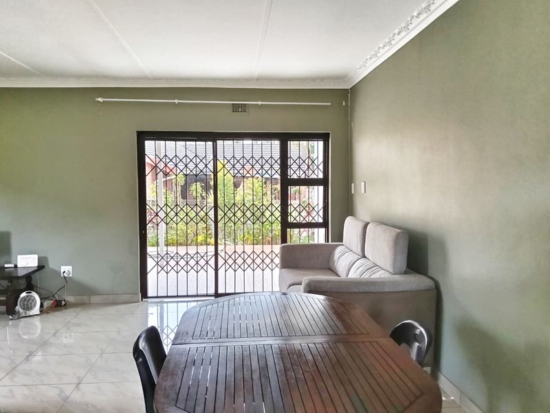 A living room featuring tiled flooring, decorative ceiling cornices, and a sliding glass door with a security gate leading to the exterior.