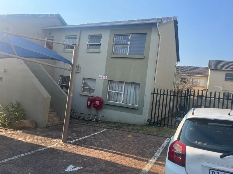 Front elevation of a two-story apartment building featuring paved parking, a shade sail, and security features including window bars and perimeter fencing.