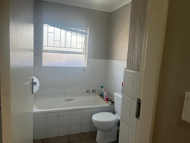 A functional bathroom featuring a built-in bathtub, toilet, and tiled splashback, requiring cosmetic updates to improve its overall condition and appeal.
