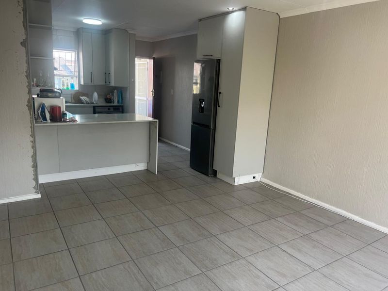 Open-plan living and kitchen area featuring neutral tiled flooring, modern cabinetry, and a functional kitchen island, offering a versatile space for daily living.