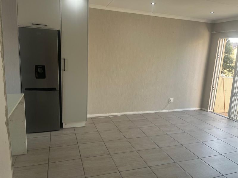 An open-plan living area featuring neutral tiled flooring, recessed lighting, and built-in cabinetry, with direct access to an outdoor balcony through a sliding door.