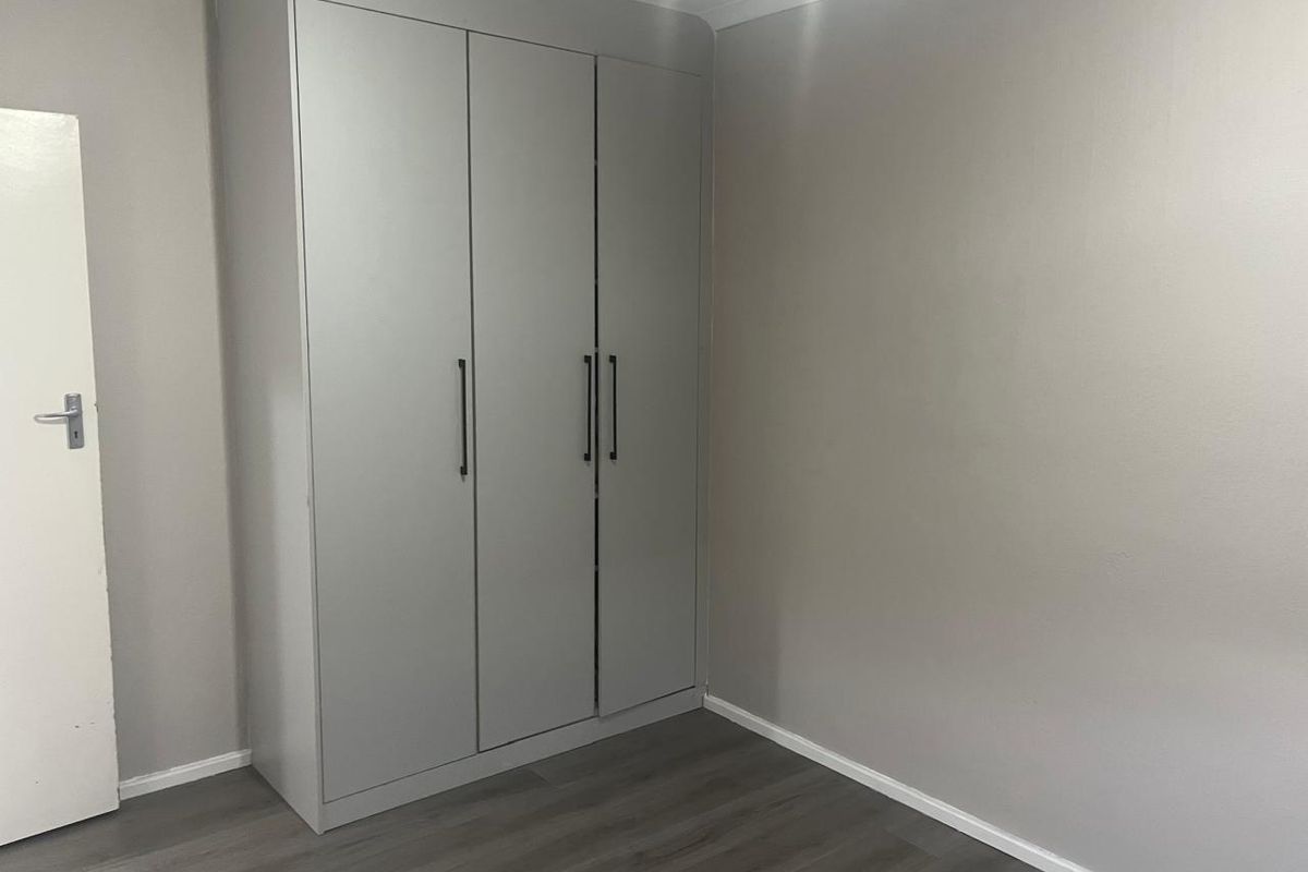 A clean, empty bedroom featuring modern grey laminate flooring and a built-in wardrobe with contemporary handles.