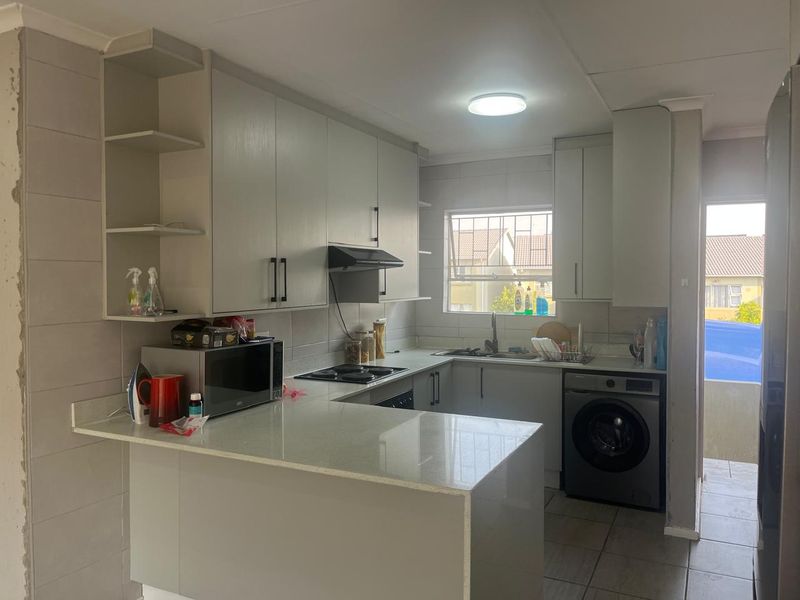 Modern kitchen featuring light grey cabinetry, stone countertops, integrated hob, extractor fan, and tiled finishes, with a functional layout and direct access to the exterior.