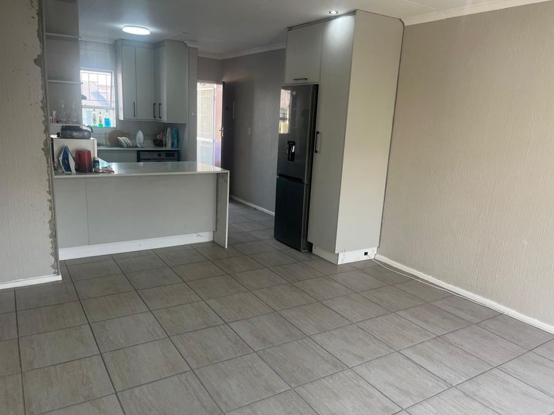 Open-plan living and kitchen area featuring neutral tiled flooring, modern cabinetry, and a breakfast bar, awaiting final finishing touches to the walls and trim.