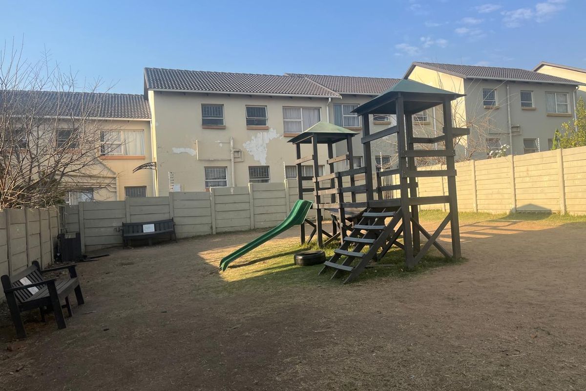 Rear communal garden area featuring a children's play structure and precast concrete boundary walls, showing signs of exterior maintenance requirements.