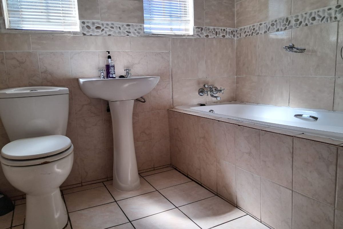 A functional bathroom featuring a pedestal basin, a built-in bathtub with wall-mounted taps, and a standard toilet, finished with neutral wall and floor tiling.