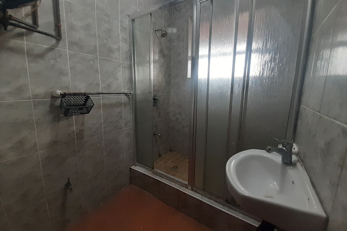 A functional bathroom featuring a shower enclosure, pedestal basin, and tiled finishes, currently in need of cosmetic updates and modernization.