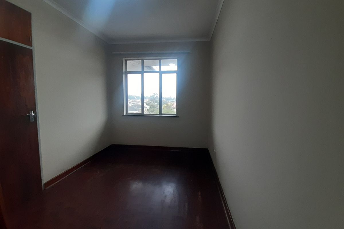 An empty bedroom featuring wooden flooring, a built-in cupboard, and a window providing natural light.
