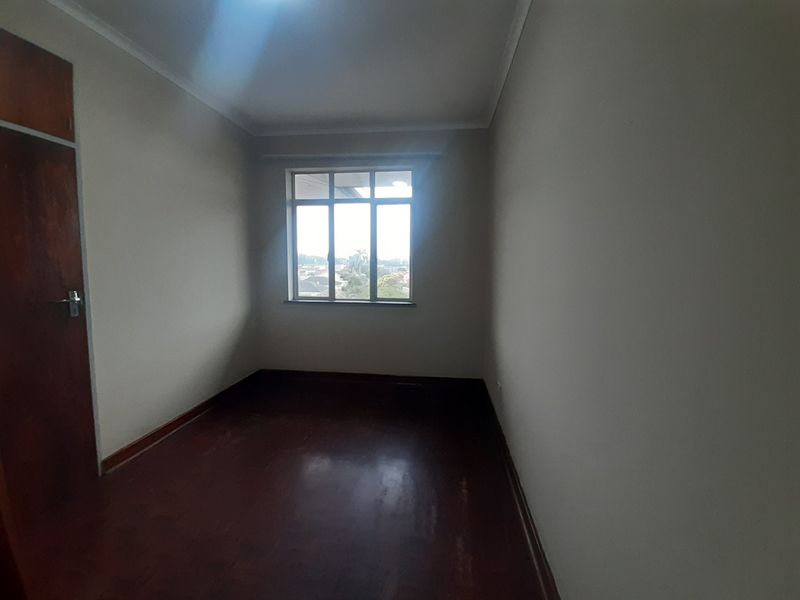 An empty bedroom featuring wooden flooring, a built-in cupboard, and a window providing natural light.