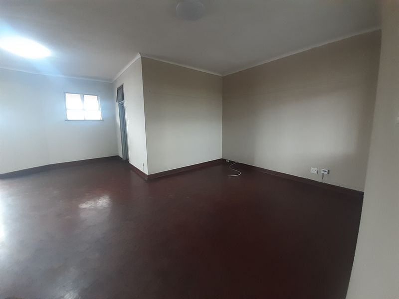 An empty, neutrally painted living area featuring dark flooring, coving, and standard electrical fixtures.