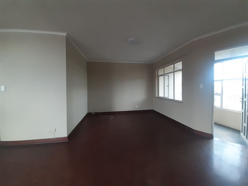 An empty living room featuring dark flooring, neutral walls, and large windows that provide natural light and access to an adjacent space.