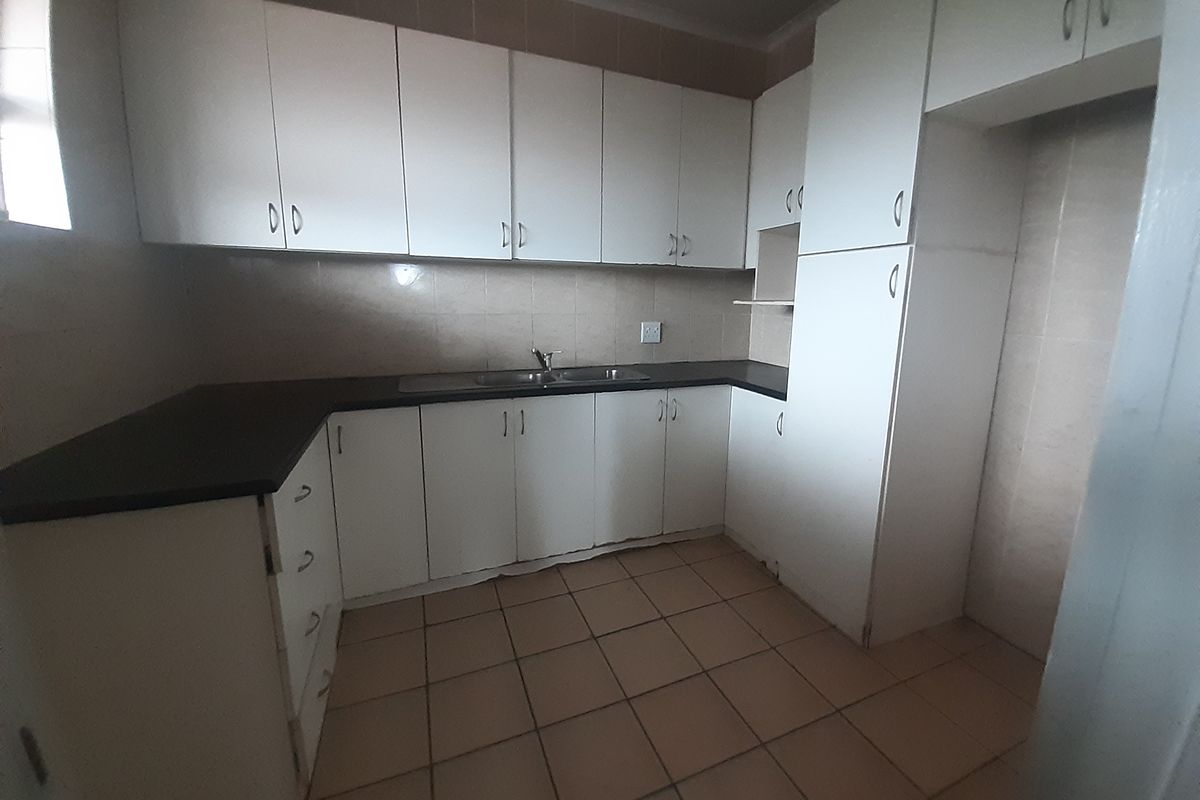 A functional, empty kitchen featuring white built-in cabinetry, dark laminate countertops, a double sink, and tiled flooring, offering a blank canvas for renovation.