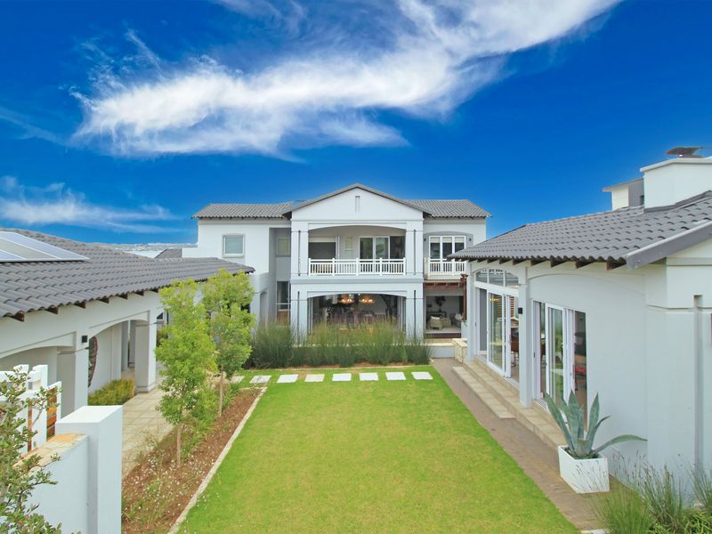 A well-maintained rear exterior view of a modern house featuring a landscaped garden, covered patio, balcony, and solar panels on the tiled roof.