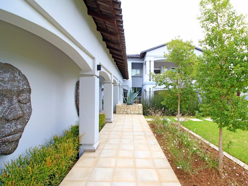 A well-maintained covered patio walkway featuring arched columns, stone planter boxes, and direct access to a landscaped garden area.