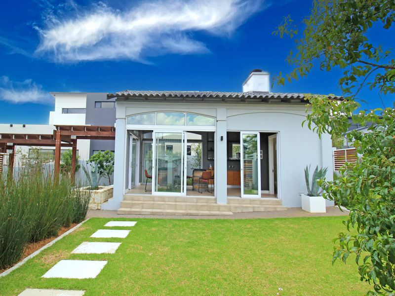 Rear view of the property featuring a landscaped garden, paved walkway, and a covered patio with sliding glass doors leading into the home.