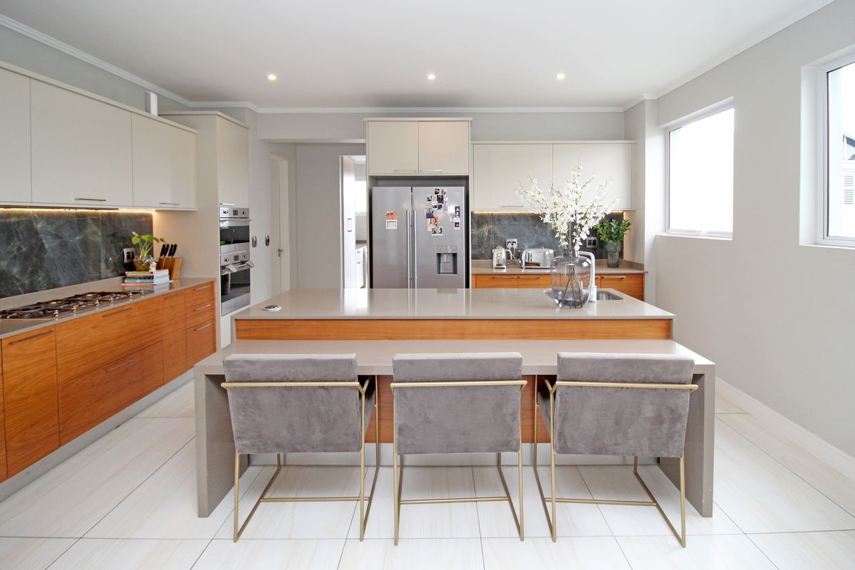 Modern kitchen featuring a large central island with breakfast bar, stone countertops, integrated appliances, and high-quality cabinetry with under-cabinet lighting.