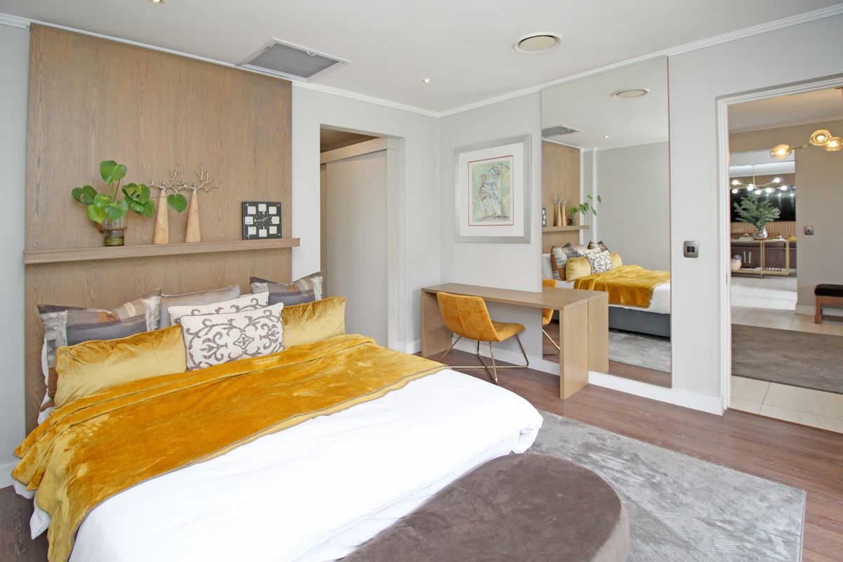 A well-appointed bedroom featuring a timber accent wall, integrated desk space, and a large floor-to-ceiling mirror, creating a bright and modern atmosphere.