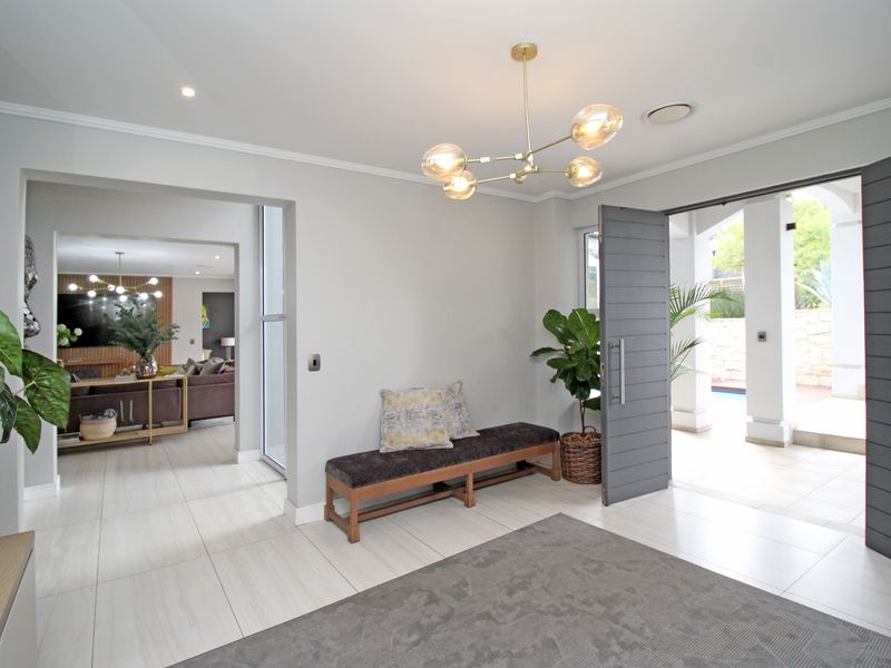 Spacious modern entrance hall featuring large format floor tiles, a contemporary chandelier, and a wide pivot door leading to an outdoor patio area.