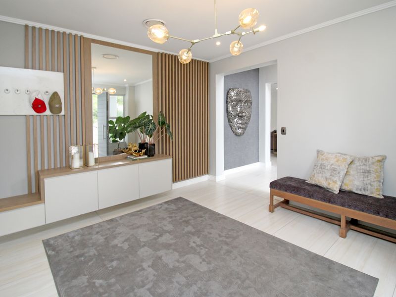 A modern, well-lit entrance hall featuring custom built-in cabinetry, a decorative timber slat wall, and elegant tiled flooring.