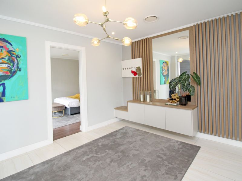 Modern entrance foyer featuring a stylish timber slat feature wall, integrated cabinetry with mirror, and contemporary lighting, leading into the home.