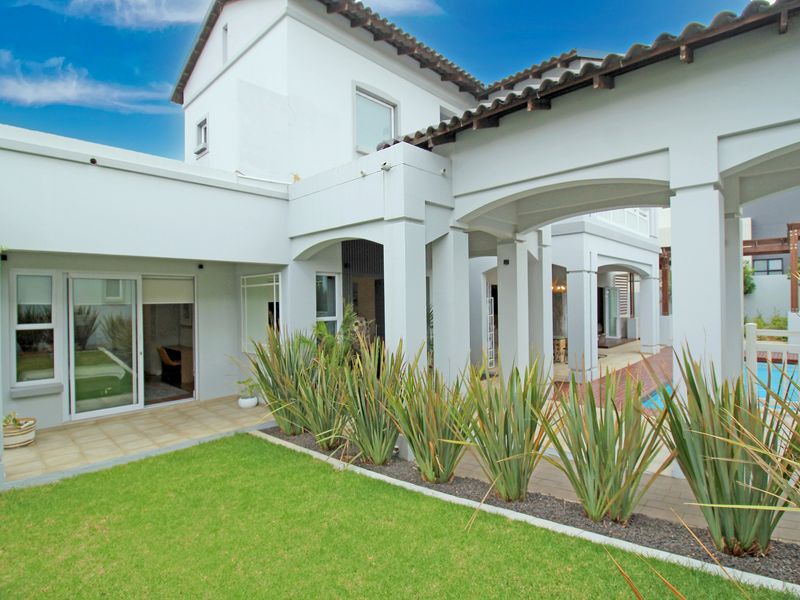 A well-maintained rear exterior view featuring a covered patio with arched columns, tiled flooring, and access to a swimming pool area.