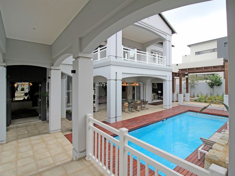 Spacious rear exterior featuring a swimming pool with timber decking, covered patio area, and a double-story structure with balcony.