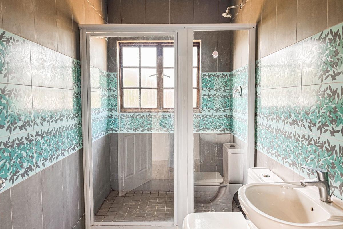 A functional bathroom featuring a shower enclosure, pedestal basin, and toilet, finished with patterned and neutral wall tiling.