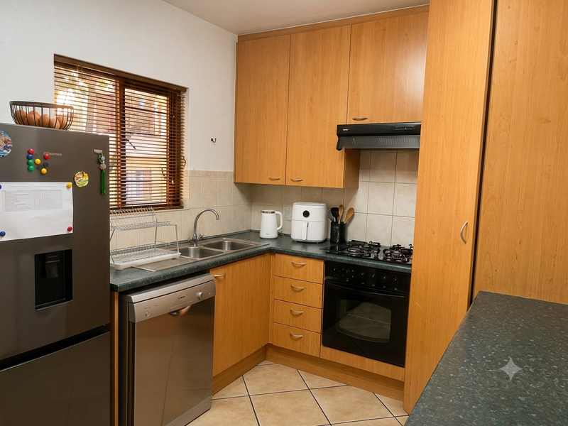A functional kitchen featuring wood-finish cabinetry, dark laminate countertops, a built-in oven with gas hob, and tiled flooring.