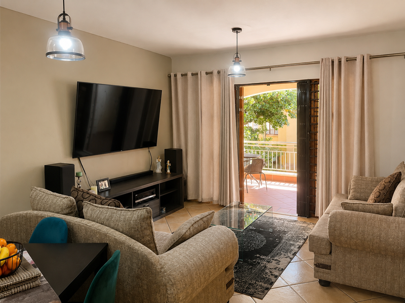 A comfortable living room featuring ceramic tile flooring, pendant lighting, and direct access to an outdoor balcony through a sliding glass door.