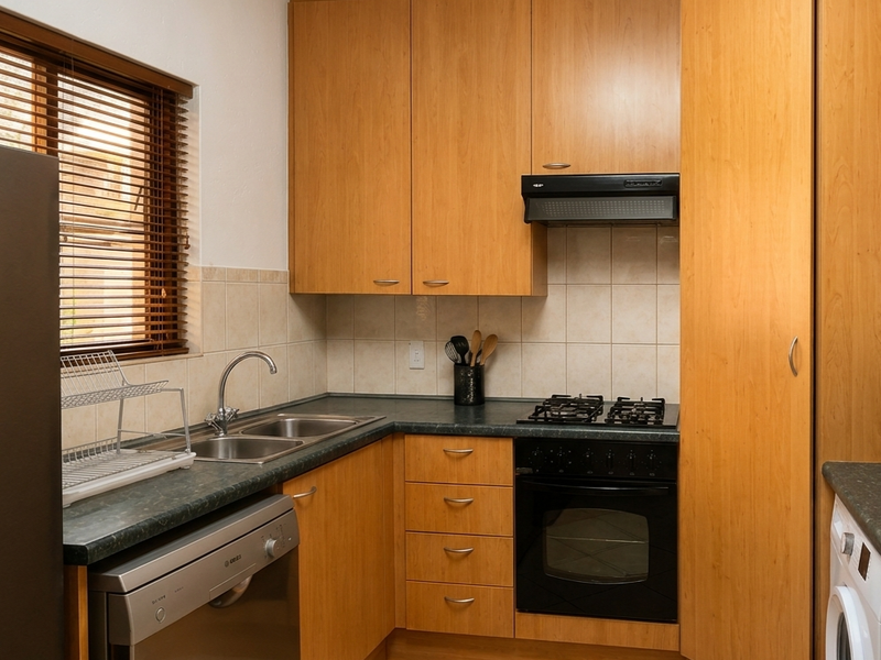 A functional kitchen featuring light wood cabinetry, dark laminate countertops, a built-in oven with gas hob, and tiled backsplash and flooring.