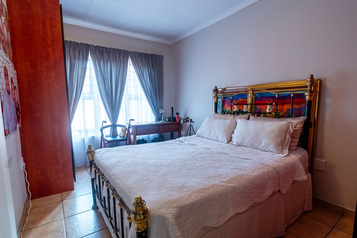 A functional bedroom featuring tiled flooring, a built-in wardrobe, and natural light through windows fitted with security bars.