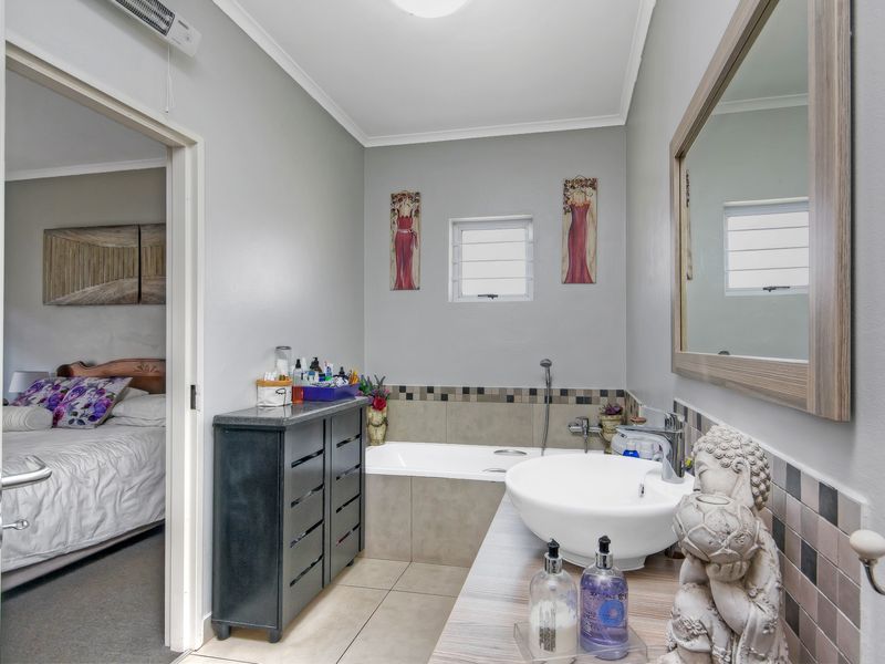 A well-maintained bathroom featuring a built-in bathtub, a modern vessel sink vanity, and neutral tiling, with direct access to an adjacent bedroom.