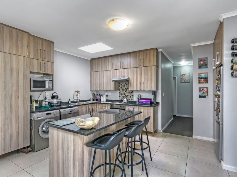A functional kitchen featuring wood-look cabinetry, granite countertops, a central island, and integrated appliances, complemented by tiled flooring and a skylight.