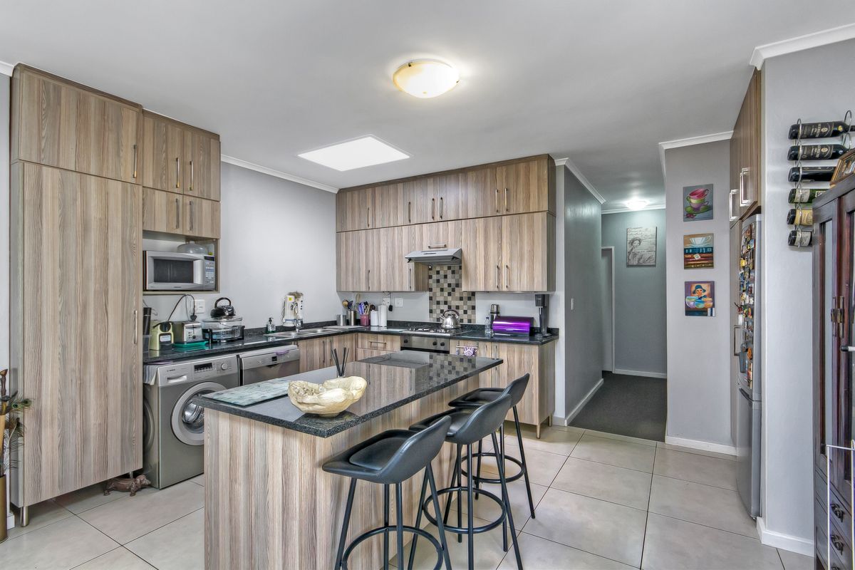 A functional kitchen featuring wood-look cabinetry, granite countertops, a central island, and integrated appliances, complemented by tiled flooring and a skylight.