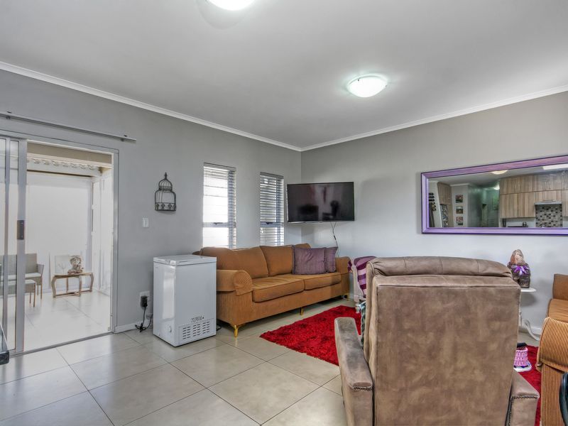 A living room featuring tiled flooring, neutral wall tones, and a sliding glass door providing access to an adjacent space.