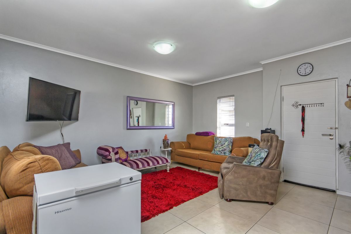 A functional living room featuring neutral tiled flooring, light grey walls, and a direct access door to the exterior.
