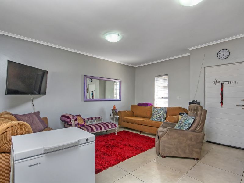 A functional living room featuring neutral tiled flooring, light grey walls, and a direct access door to the exterior.