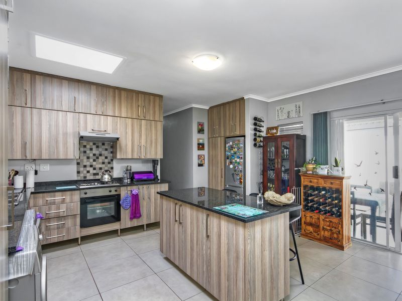 Modern kitchen featuring wood-finish cabinetry, granite countertops, a central island, built-in oven and hob, and a skylight for natural light.