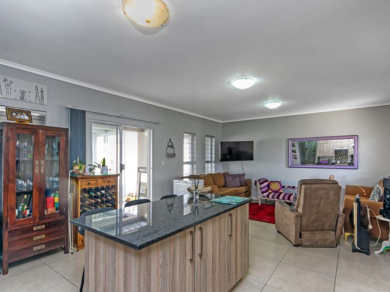 Spacious open-plan living area featuring a central kitchen island with granite countertops, tiled flooring, and sliding glass doors leading to the patio.