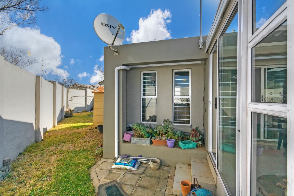 Rear exterior view of the townhouse featuring a paved patio area, sliding glass doors, and a private garden space with boundary walling.
