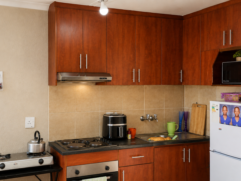 A functional kitchen featuring wood-finish cabinetry, tiled backsplash, built-in oven, and electric hob, providing essential cooking and storage space.