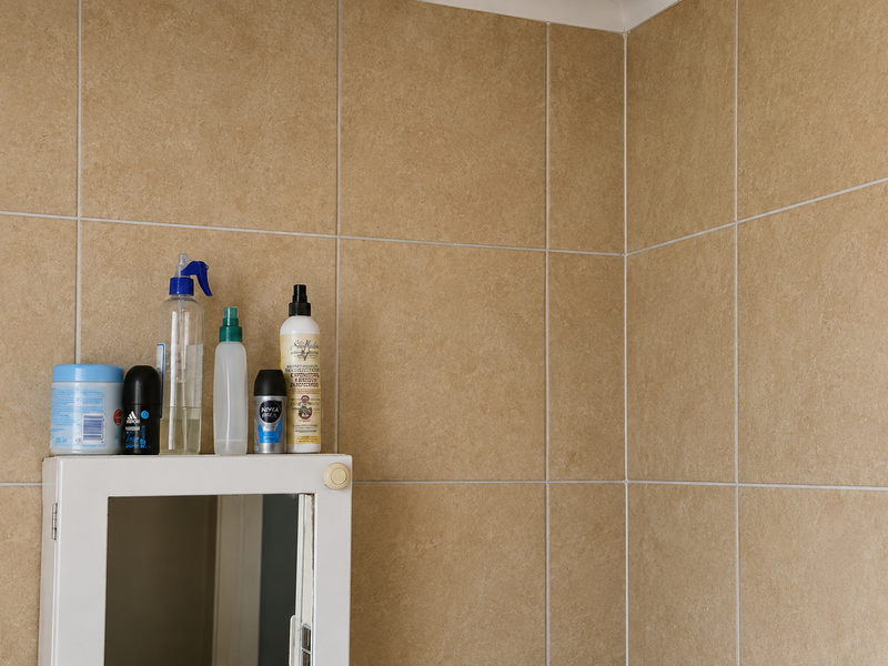 A close-up view of a bathroom wall featuring neutral-toned ceramic wall tiles and a white medicine cabinet.