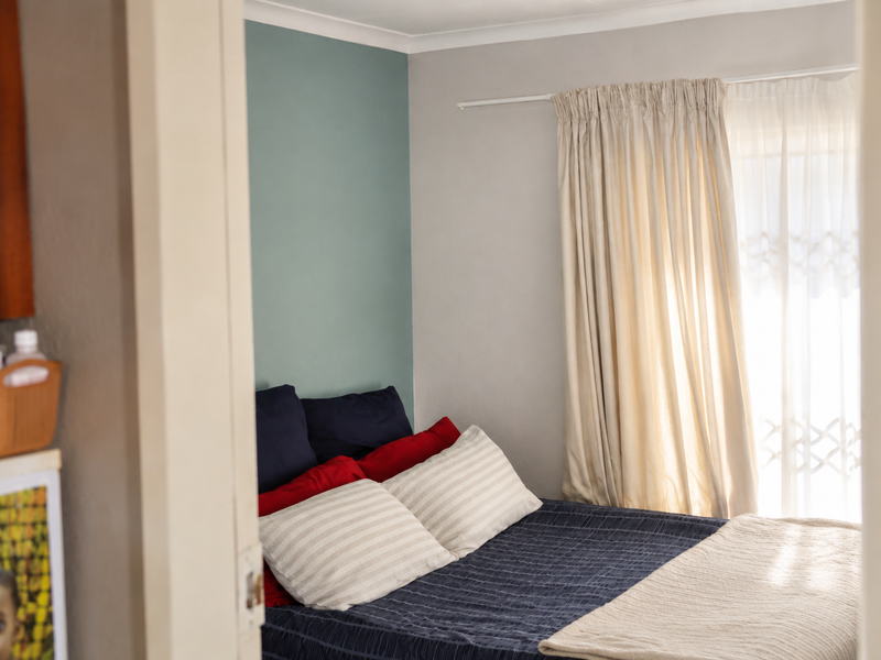 A view into a bedroom featuring a neutral color palette with a soft green accent wall and natural light from the window.