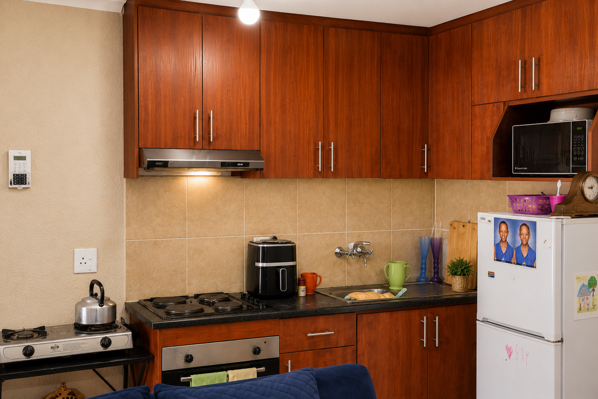 A functional kitchen featuring wood-finish cabinetry, tiled backsplash, built-in oven, extractor fan, and integrated microwave storage, providing a practical workspace.