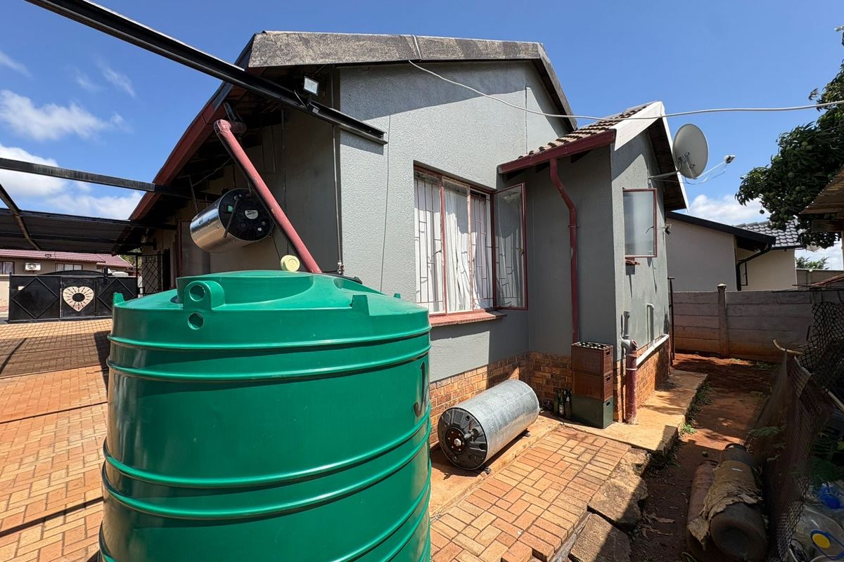 Rear exterior view of the house featuring a large water storage tank, paved courtyard area, and exposed utility infrastructure.