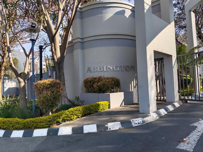 The entrance to the Abbington complex featuring a secure gate, paved driveway, and well-maintained landscaped garden beds.