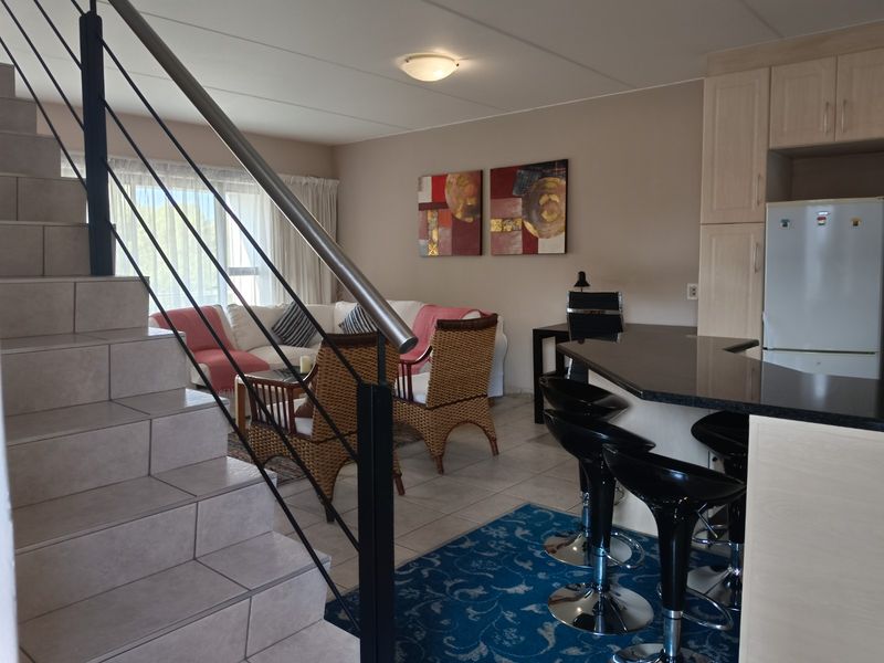 Open-plan living area featuring a tiled staircase with a modern handrail, integrated kitchen cabinetry, and a granite breakfast bar.