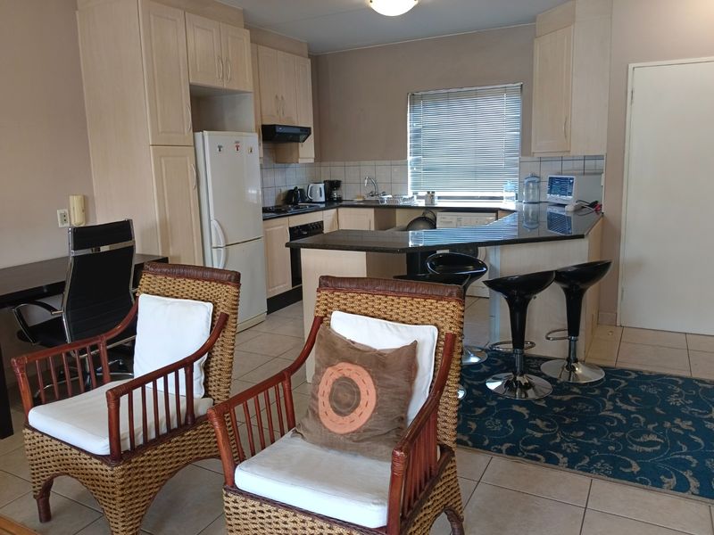 Open-plan kitchen featuring light wood cabinetry, granite countertops, and integrated appliances, seamlessly flowing into the living area with tiled flooring throughout.